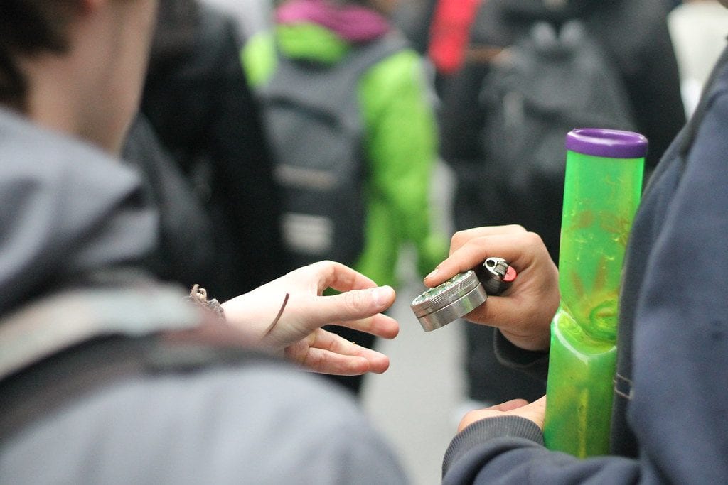 man with a bong and electric weed grinder handing the electric grinder to another person