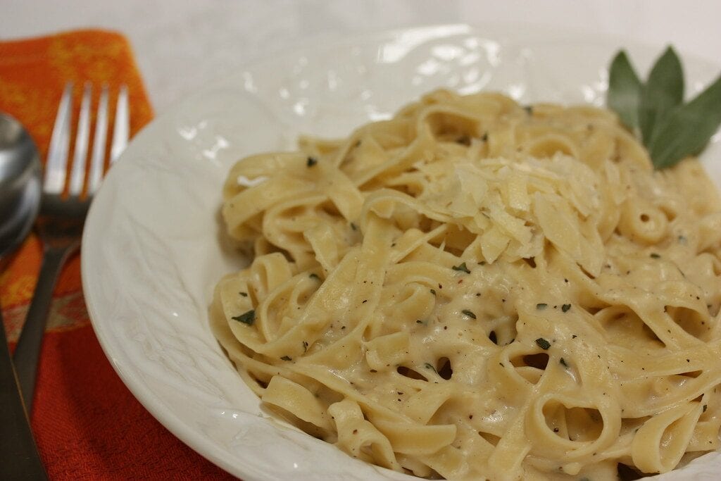 fettuccine alfredo on a white plate. The spice is on top of the pasta. Some green leaves on the side of the plate for decoration.