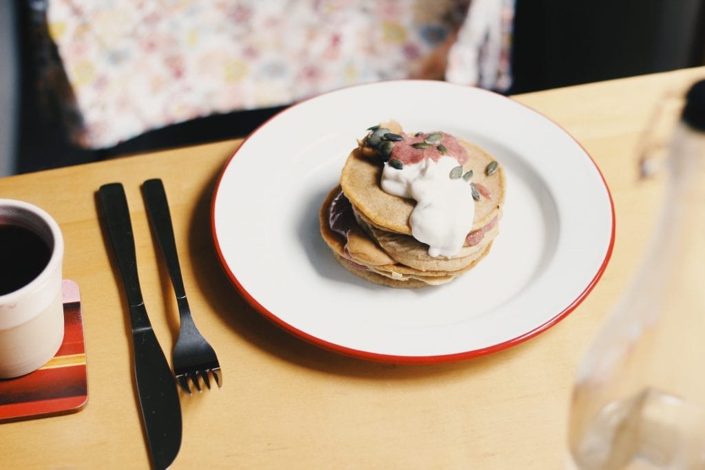 Cannabis Pancakes on a white plate with a knife and fork beside them on a wooden table. A perfect weed breakfast edible.