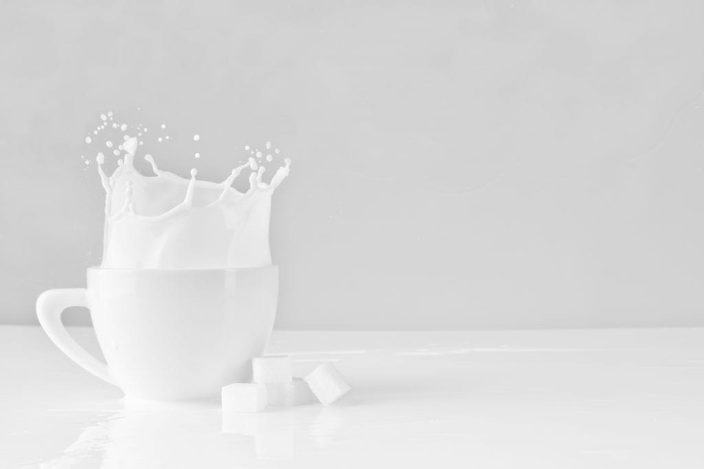 glass of milk in a white mug. The milk is splashing over the sides. 