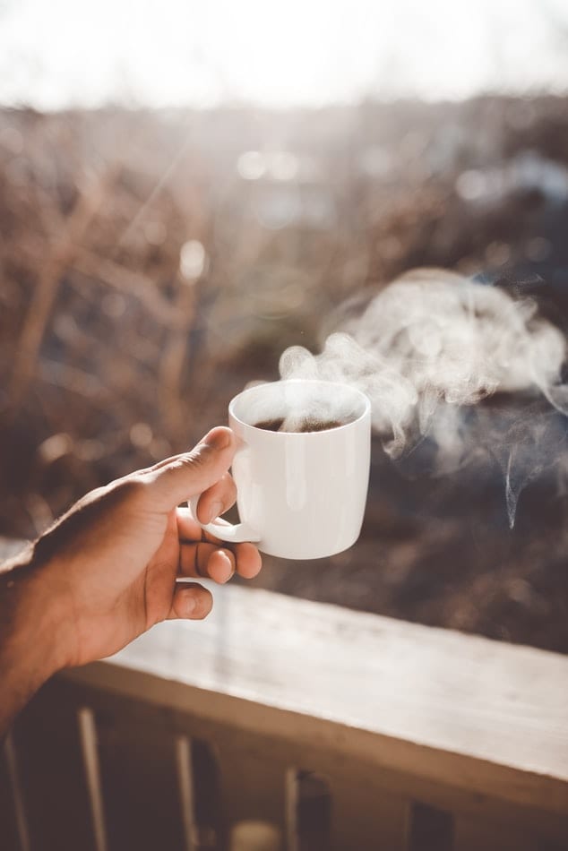 a man holding a hot steaming cbd coffee that is in a white mug. The steam of the coffee fills the air. 