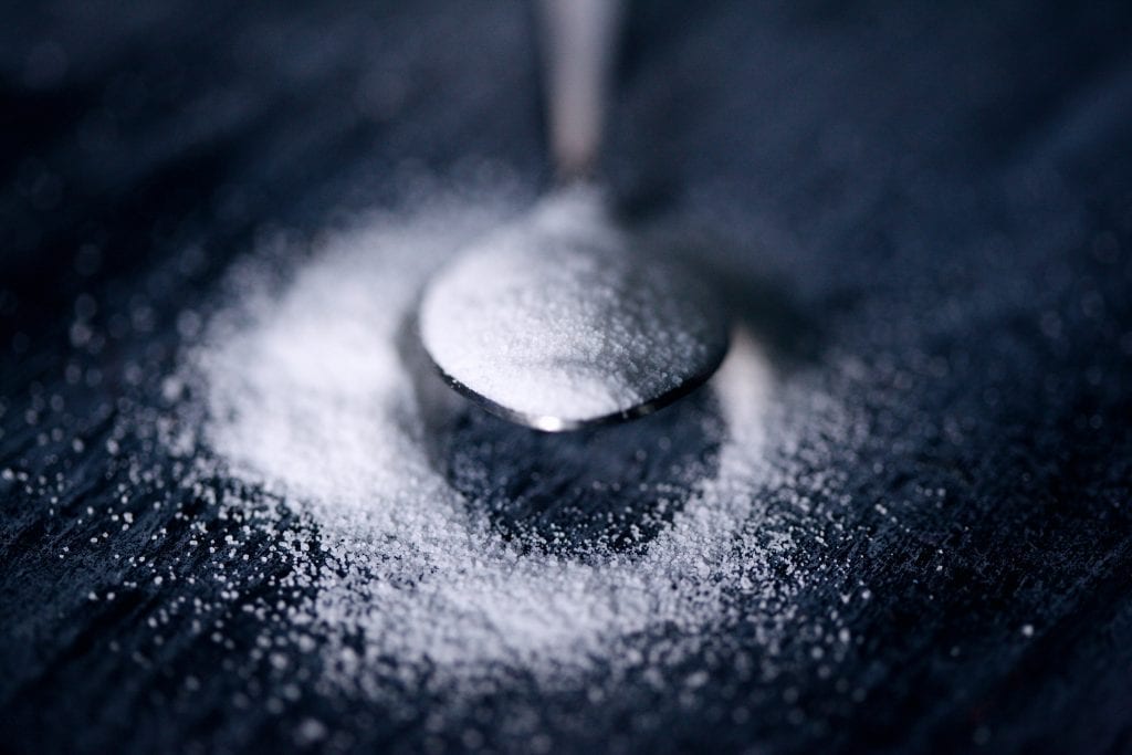 Cannabis infused sugar in a spoon. The weed sugar is overflowing onto a black table