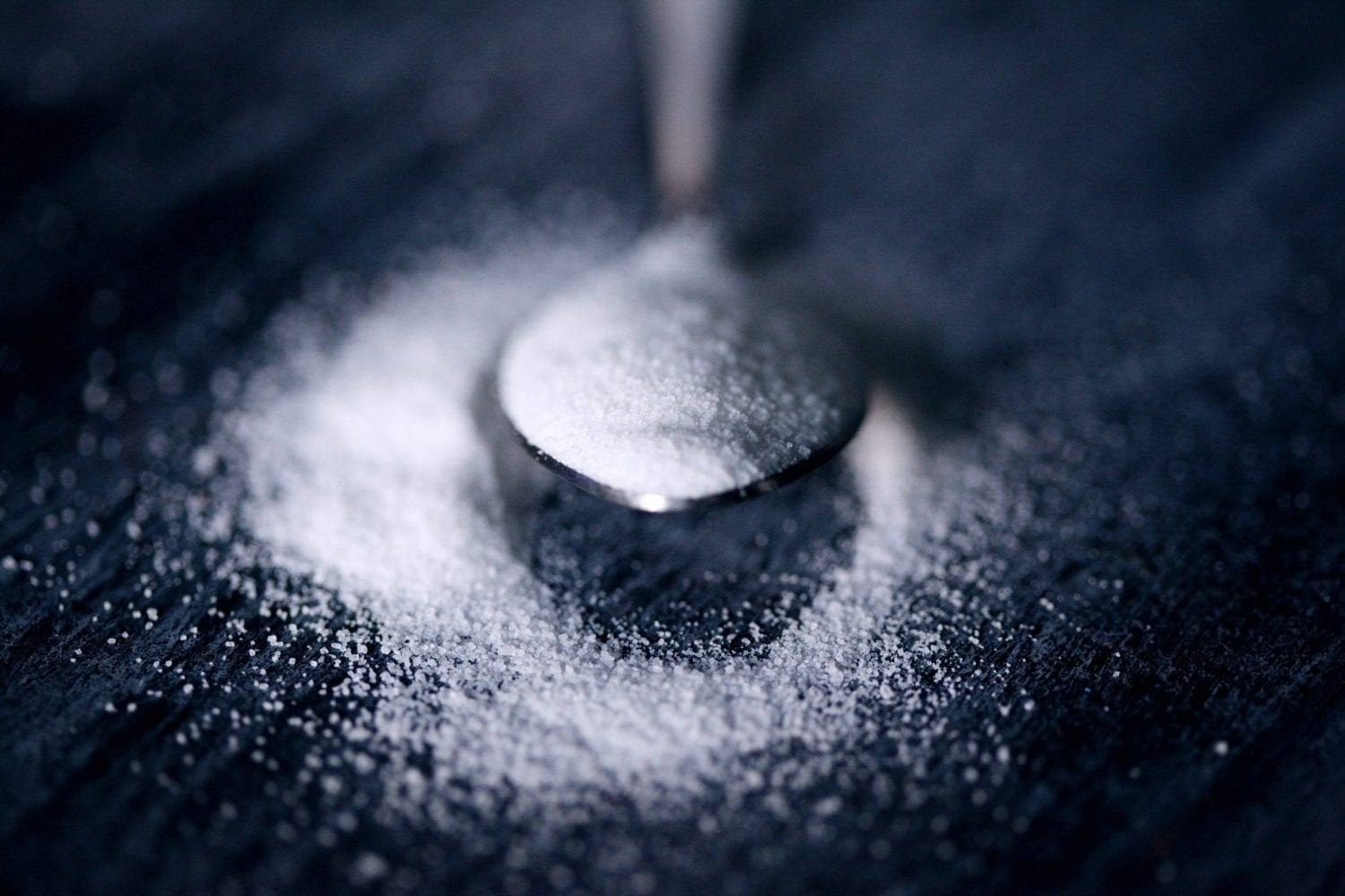 Cannabis infused sugar in a spoon. The weed sugar is overflowing onto a black table