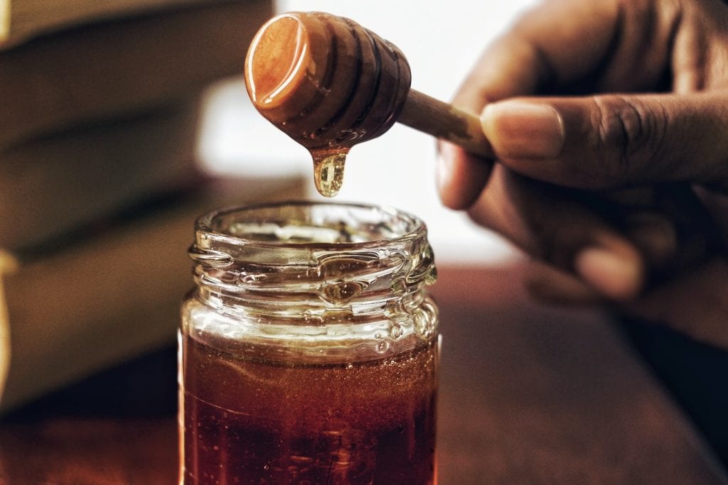 cannabis infused honey. the yellow glazed honey is dripping off the stir stick.