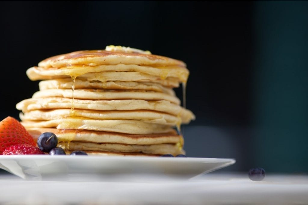 weed pancakes stacked on top of each other on a plate with butter melting overtop of them. White plate and black background