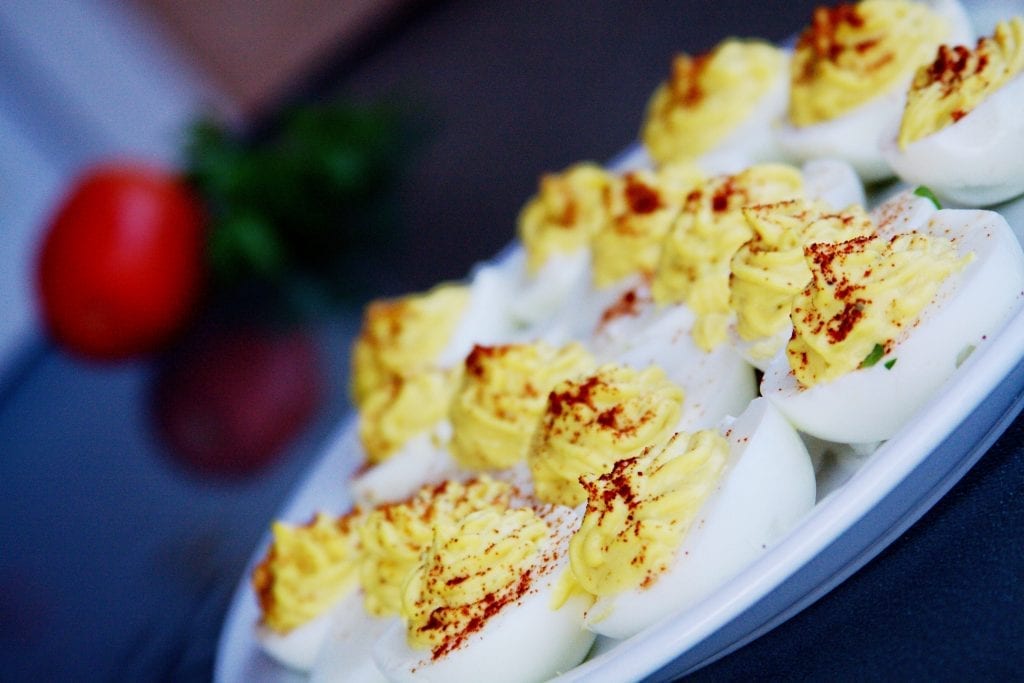 cannabis infused devilled eggs with paprika sprinkled over them. tomato in the background out of focus