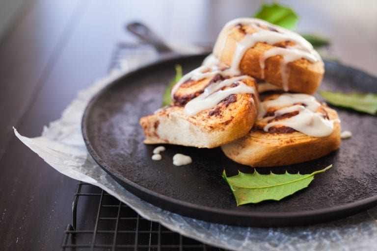 cannabis infused cinnamon rolls on a black plate with leaves beside them.