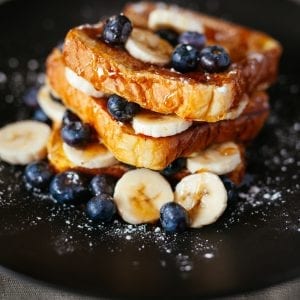 french toast on a black plate with blueberries, bananas, sugar