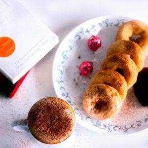 cannabis infused donuts on a white plate with jam and chocolates beside them. Kief coffee with brown sugar beside the plate on a table with 2 books along side