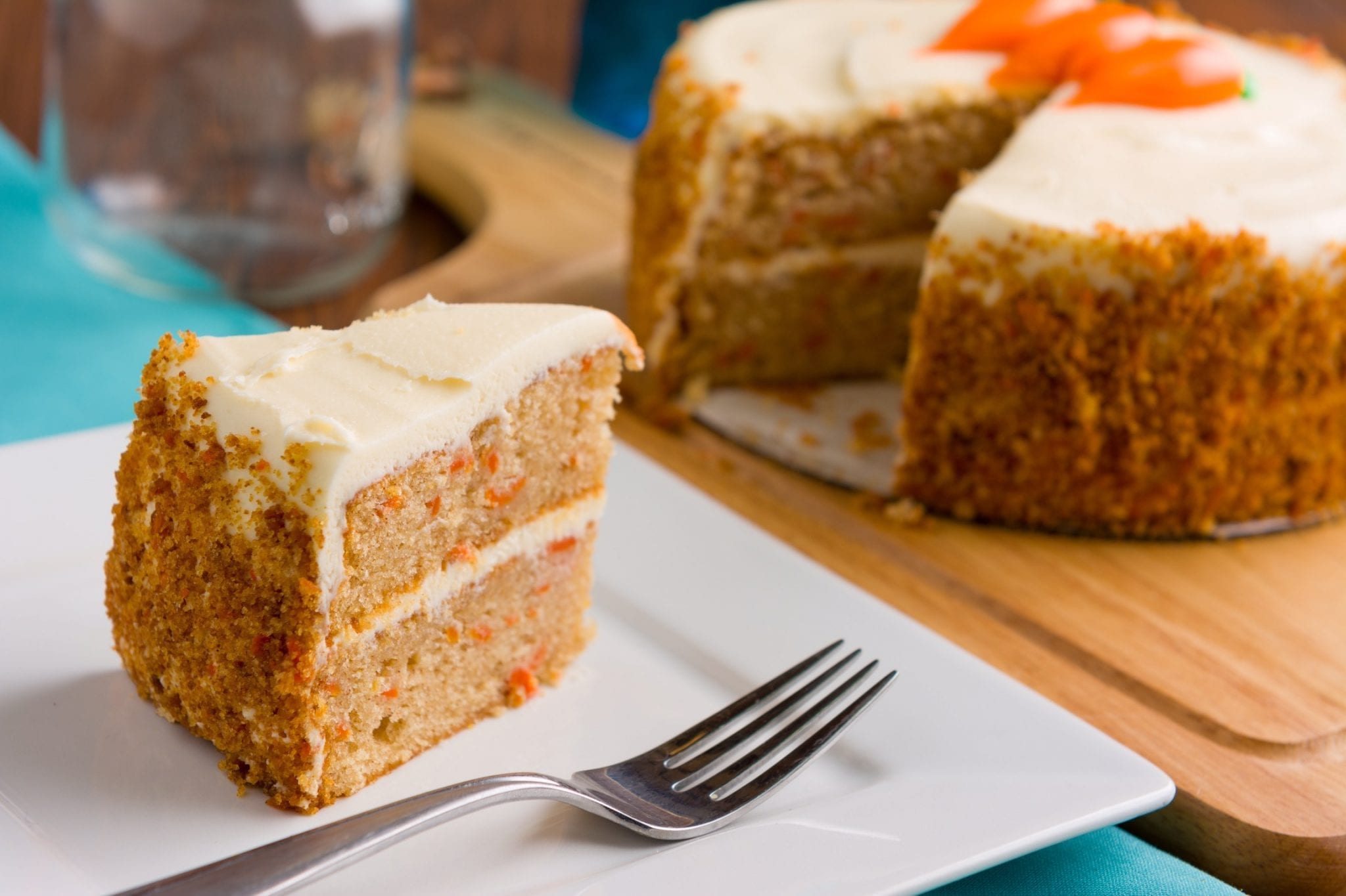 Cannabis infused carrot cake on a wooden cutting board with a slice being taken from it