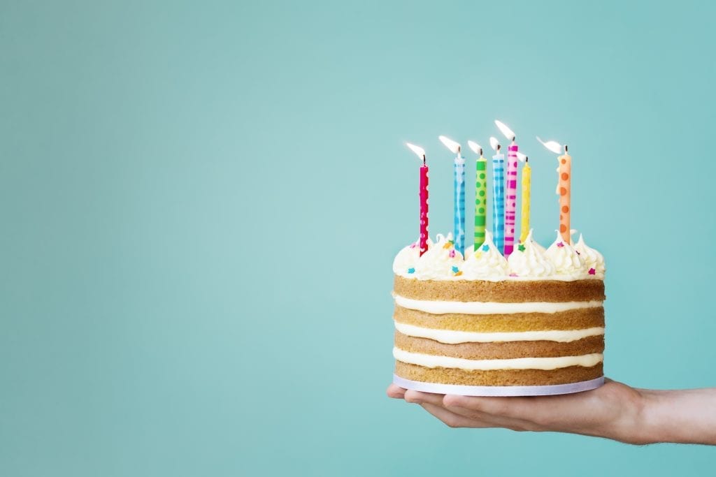 Weed birthday cake with buttercream and colourful candles in a persons hand in front of a blue wall