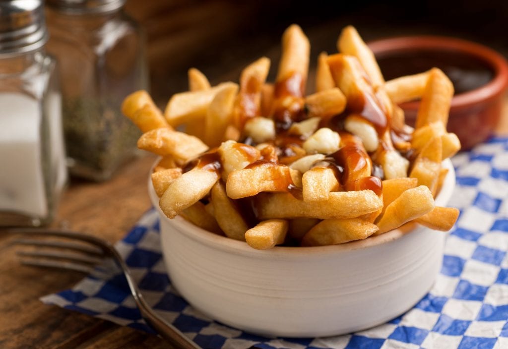 close up image of cannabis infused poutine on blue checkered tablecloth with a fork beside it and salt and pepper beside them