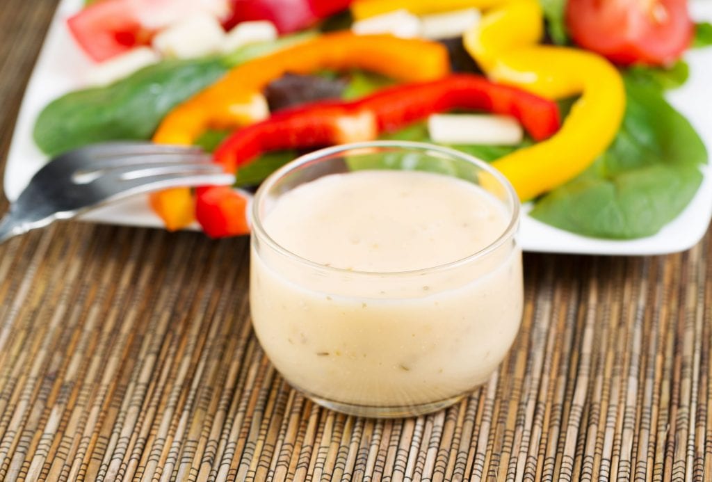 cannabis infused salad dressing in a cup with salad and a fork in the background