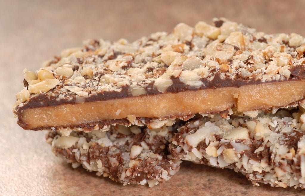 Homemade infused Chocolate English Toffee Topped with Nuts stacked on other pieces of toffee on a brown table