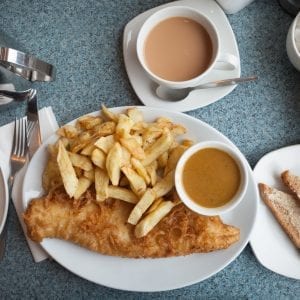 overhead shot of weed fish and chips on a white plate with a cup of coffee in the background. Marshmallows, toast, and more fish in the background