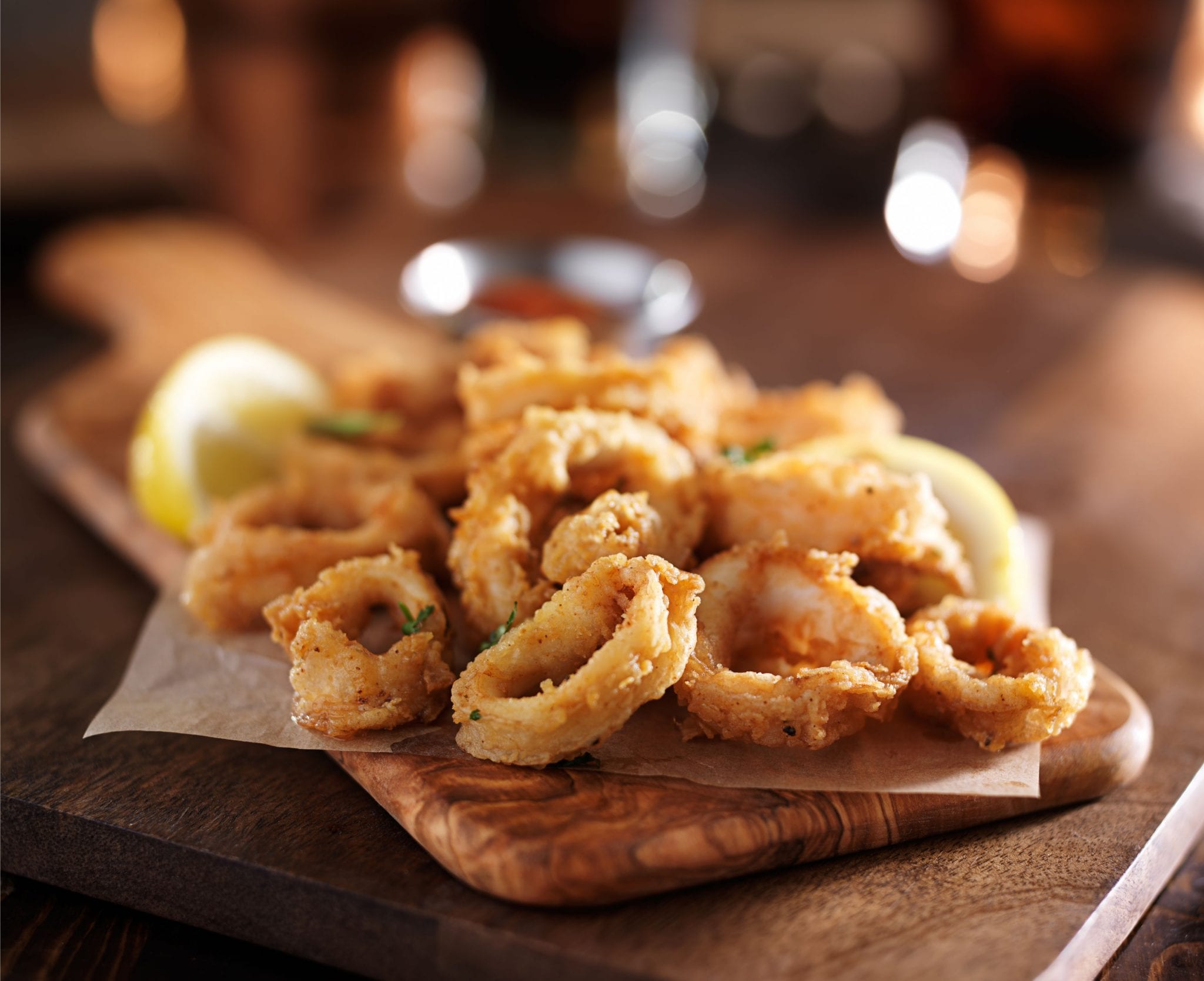 cannabis infused fried calamari rings on a wooden cutting board with a lime in the background out of focus