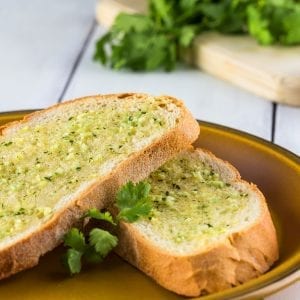 two slices of cannabis infused garlic bread on a brown plate with parsley on a cutting board in the background