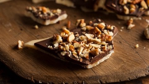 Homemade weed Chocolate English Toffee Topped with Nuts on a brown cutting board with more toffee in the background