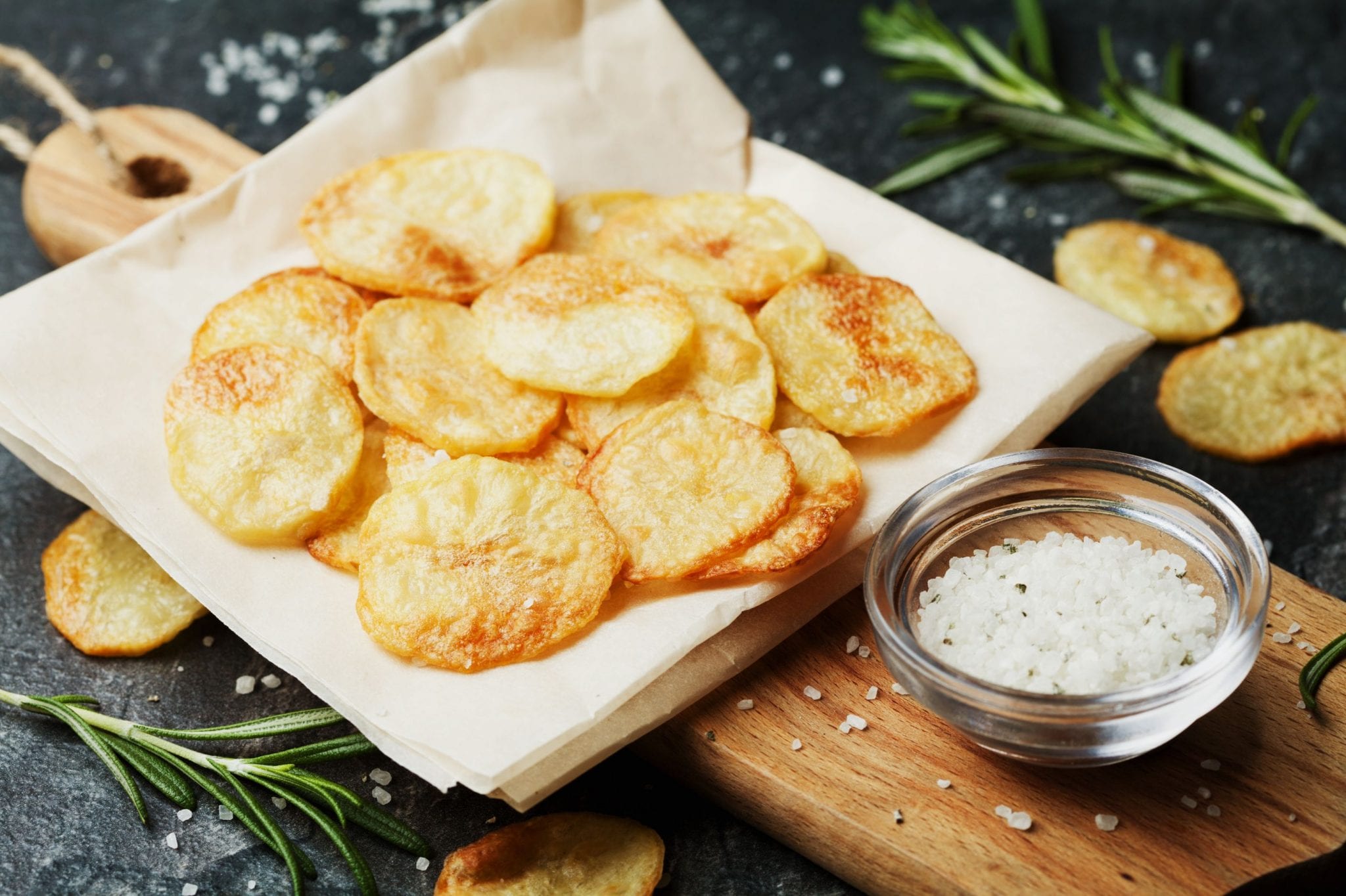 Cannabis infused potato chips and napkins which on top of the wooden cutting board with a cup of salt beside them