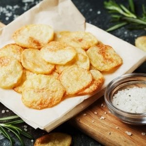 Cannabis infused potato chips and napkins which on top of the wooden cutting board with a cup of salt beside them