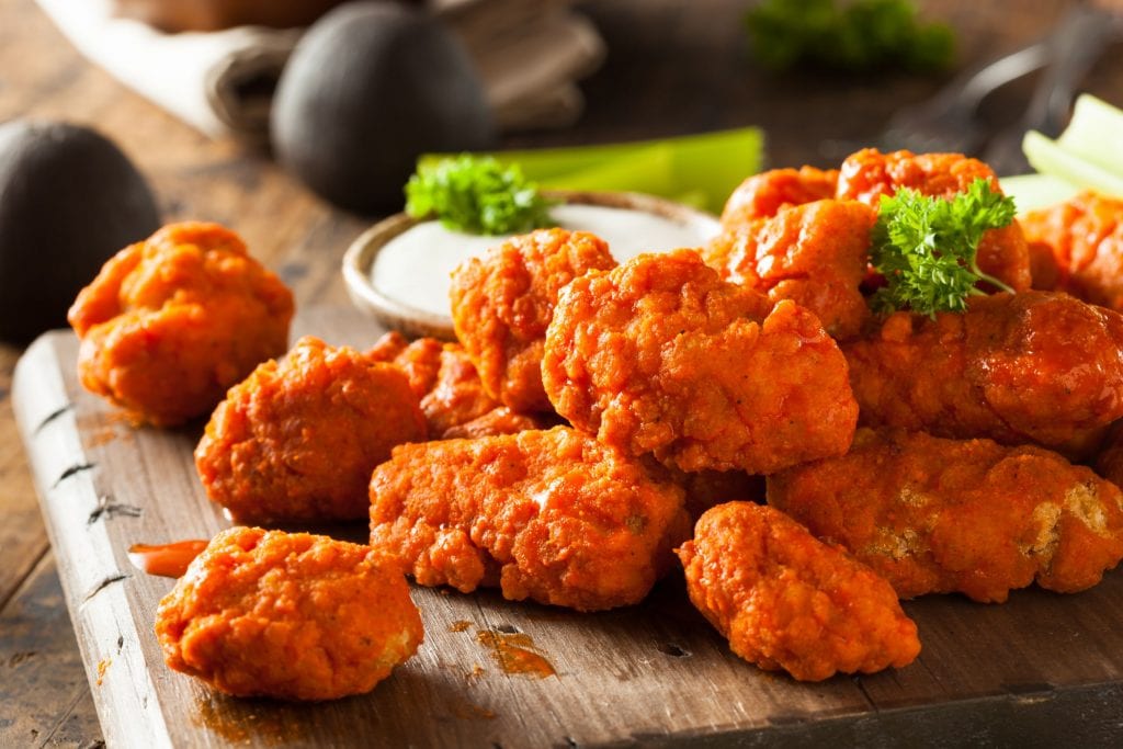 A wooden cutting board with lots of spicy cannabis infused buffalo wings with dipping sauce in the background. A weed edible dinner recipe.