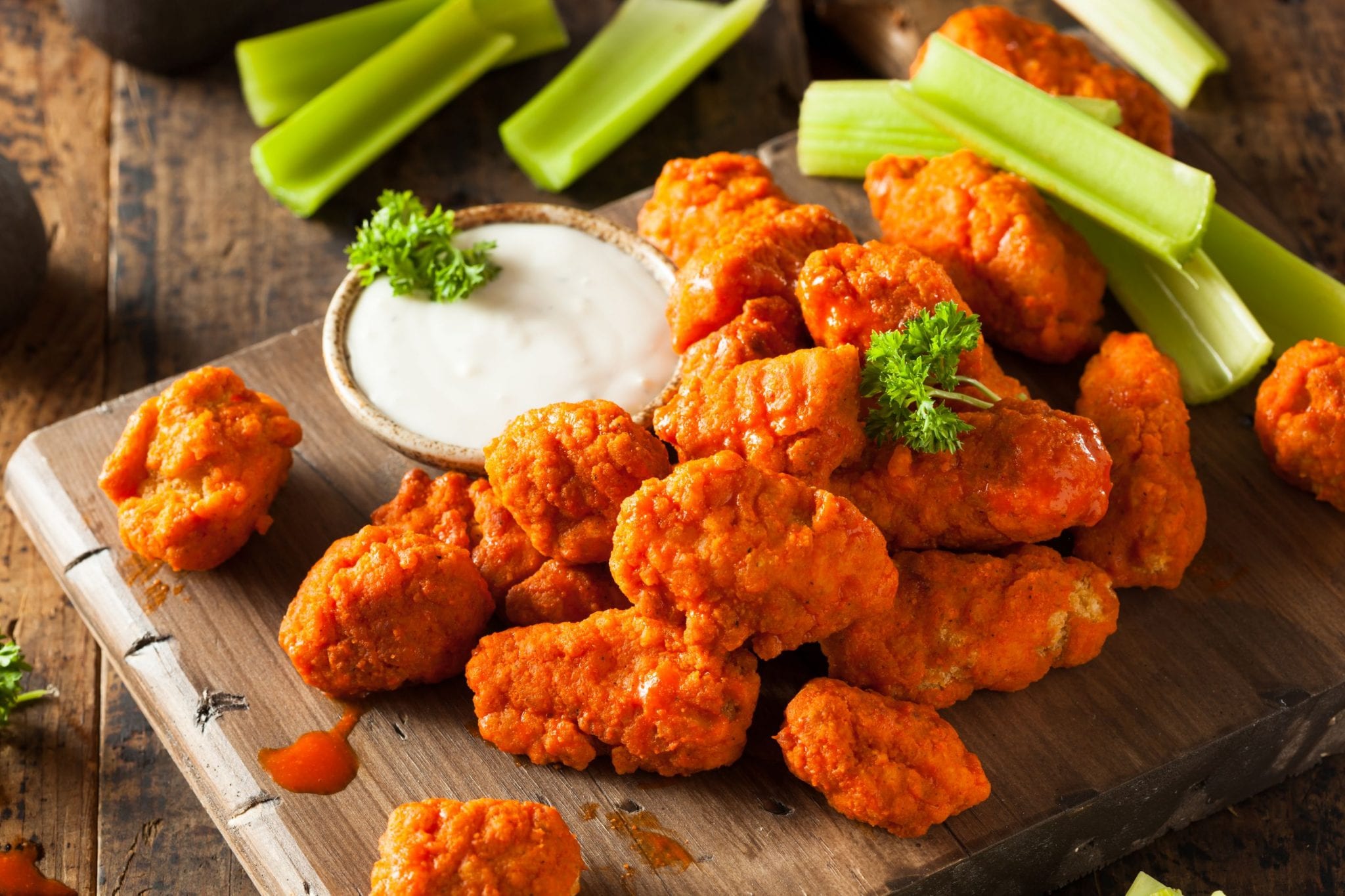 Overhead image of weed boneless buffalo wings on a wooden cutting board with dipping sauce beside the cutting board