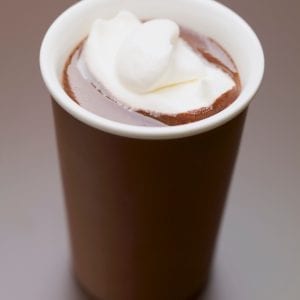 cannabis infused hot chocolate with whip cream and marshmallows on top of it. The cup is in front of a brown background