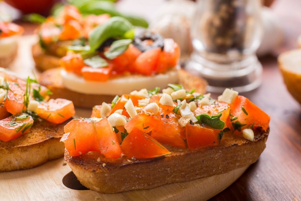 A slice of cannabis infused bruschetta I wooden cutting boardWith lots of other pieces of weed bruschetta in the background