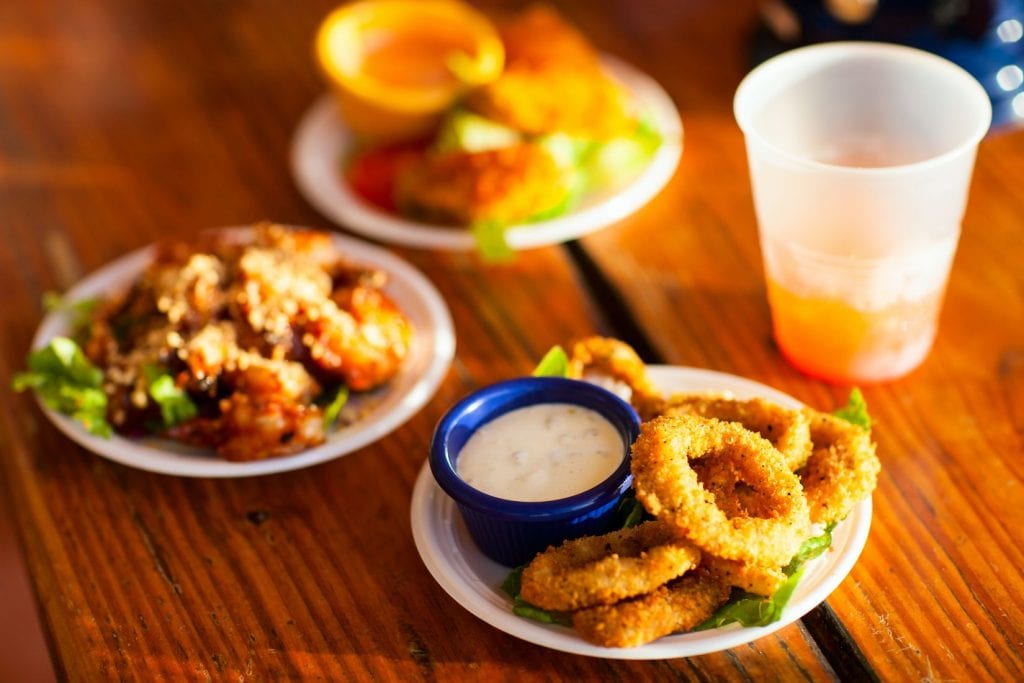 Three plates and a plastic cup with liquid in it. One of the plates as weed infused onion rings on it with dipping sauce