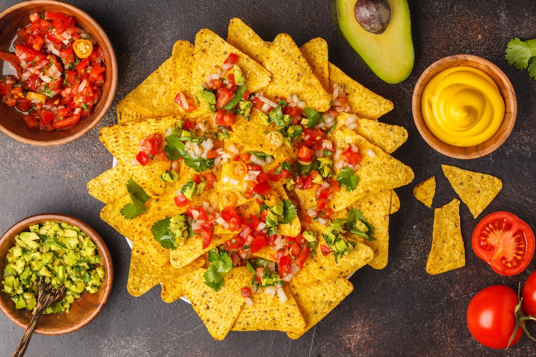 Cannabis infused nachos with guac, salsa, weed cheese, tomatos, and jalapeno's scattered around on the table