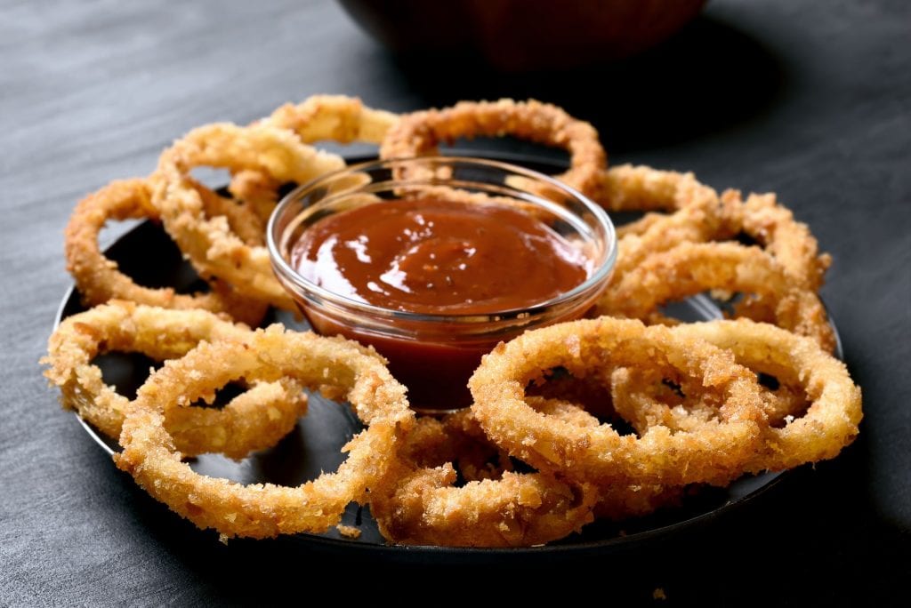 A black plate with catch up in the middle. There is weird onion rings spread artistically around the