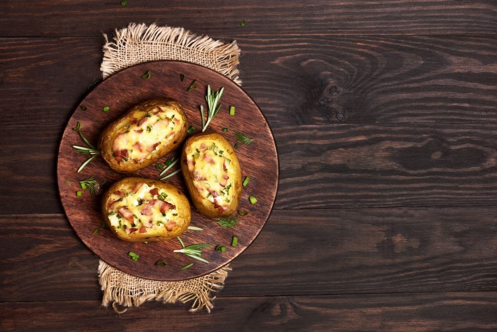 Three cannabis infused baked potatoes on a wooden cutting board with chives spread artistically on the current board