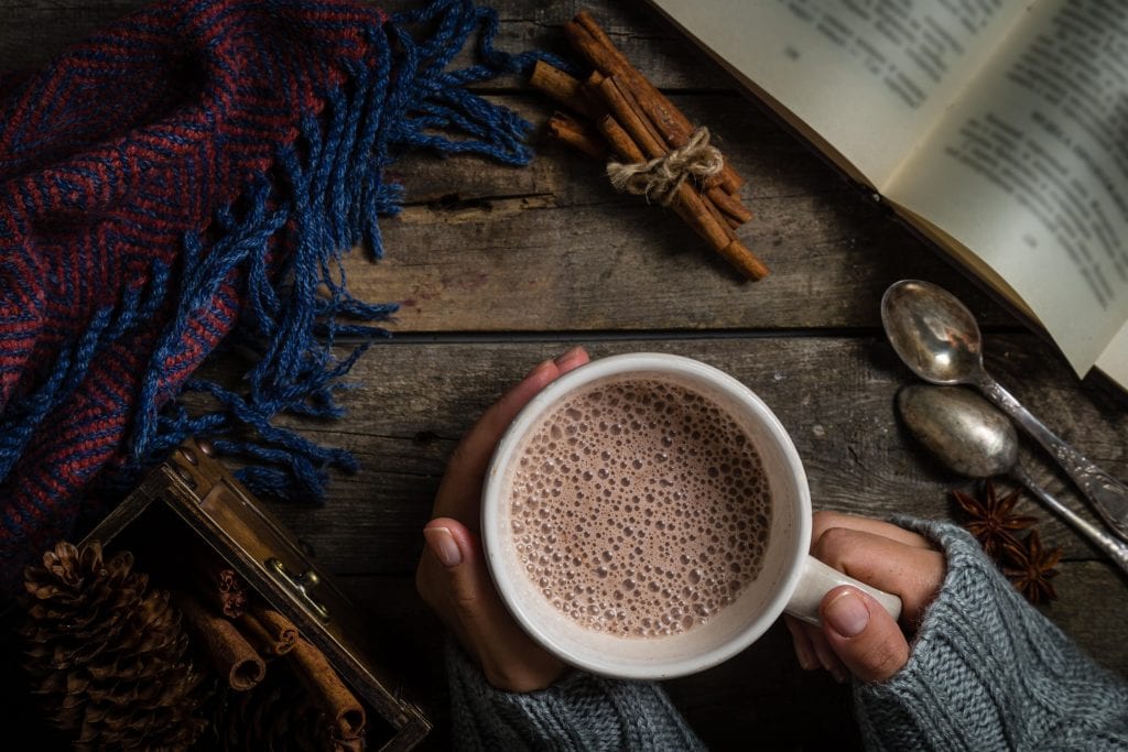 Overhead shot of a person hoding a cup of cannabis infused hot chocolate on a wood surface