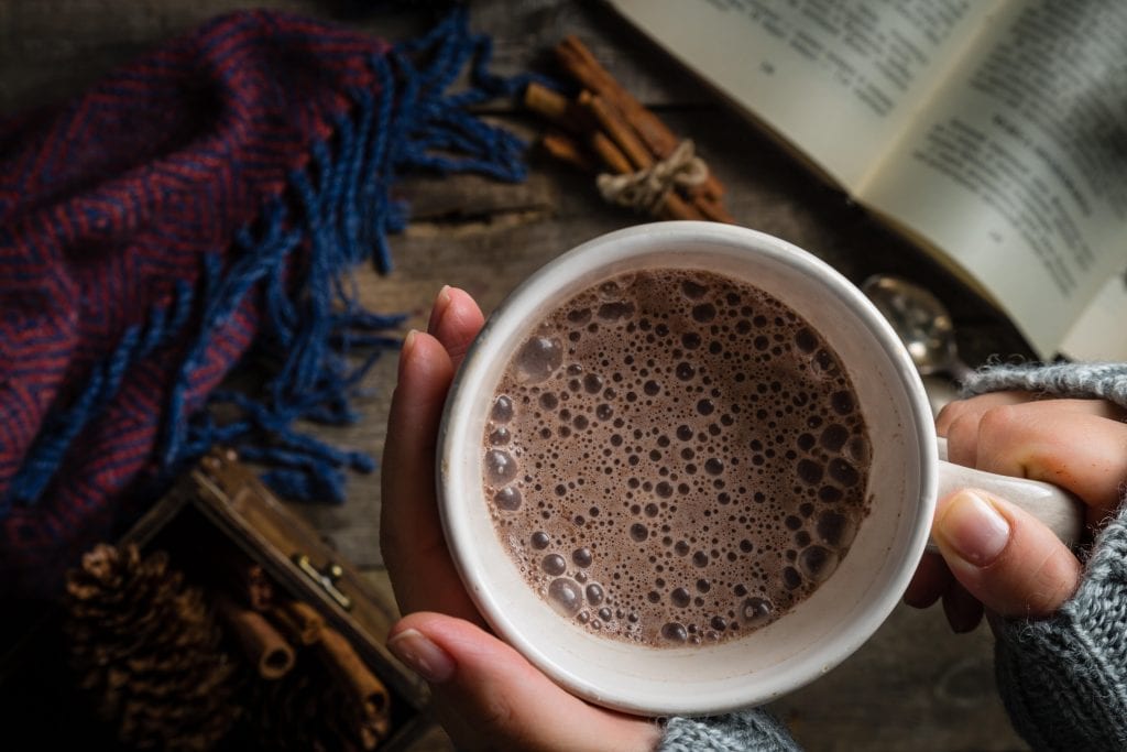 Overhead macro close up of a womans hand holding a cup of cannabis infused hot chocolate on a rustic background