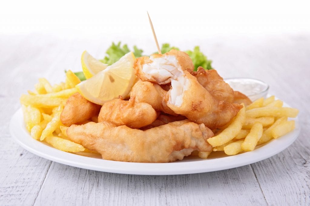 weed fish and chips on a white plate with lemon and salad in the background. A weed edible dinner recipe.