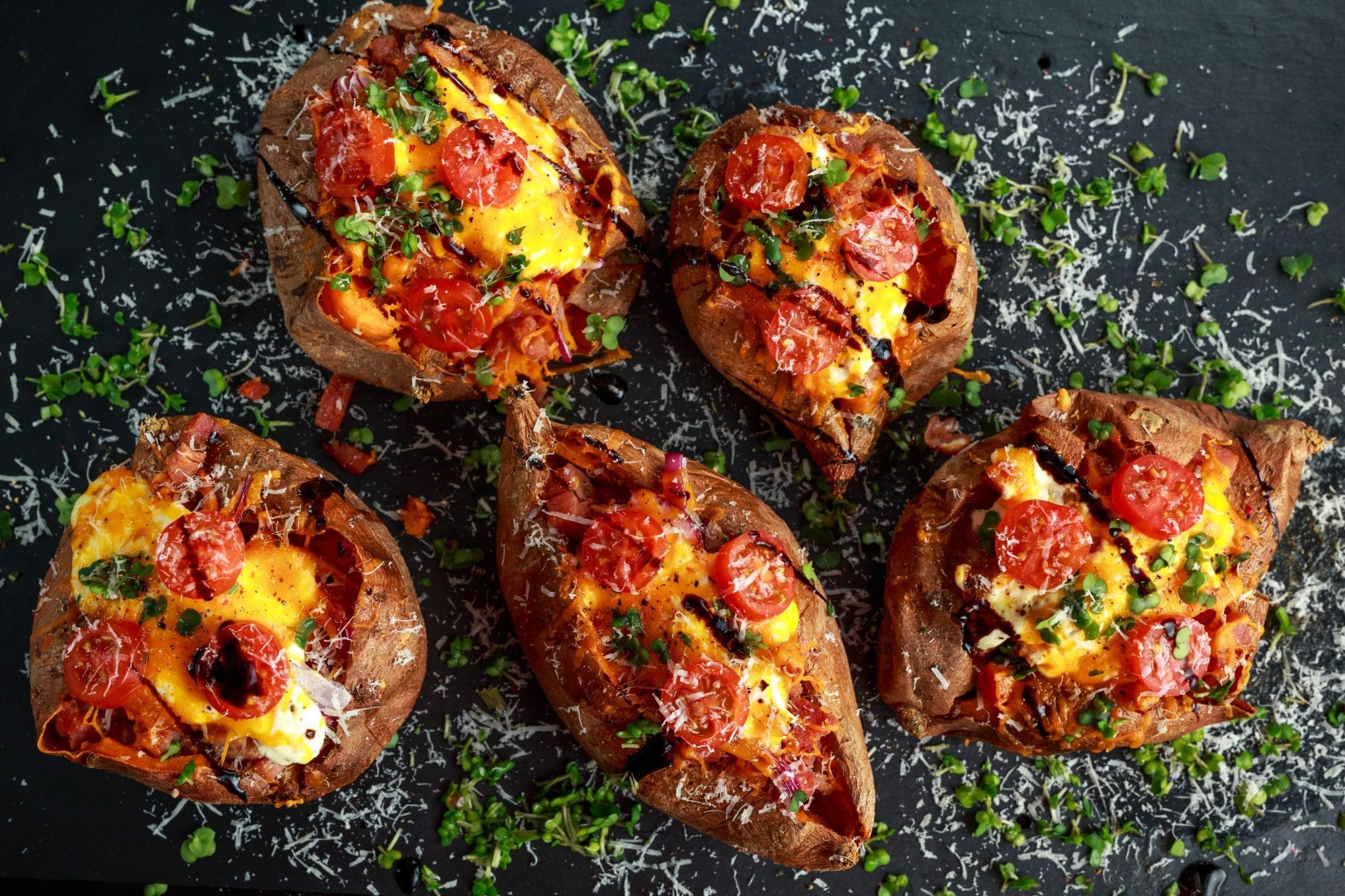 Overhead shot of five weed baked stuffed potatoes With lots of tomatoes and Parmesan cheese sprinkled over top of them