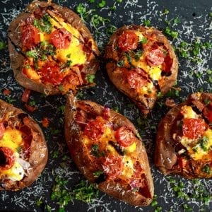 Overhead shot of five weed baked stuffed potatoes With lots of tomatoes and Parmesan cheese sprinkled over top of them