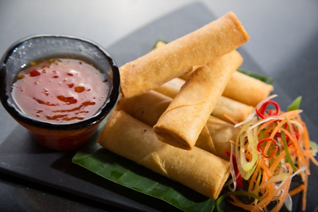 For cannabis infused spring rolls on a black plate with two Kabah spring rolls make it a TP on top of them. Sweet-and-sour sauce and veggies beside the spring rolls on the plate