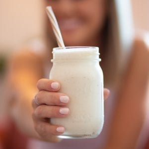 Woman holding a jar filled with cannabis infused banana smoothie Woman has pink nail polish and is out of focus in the background