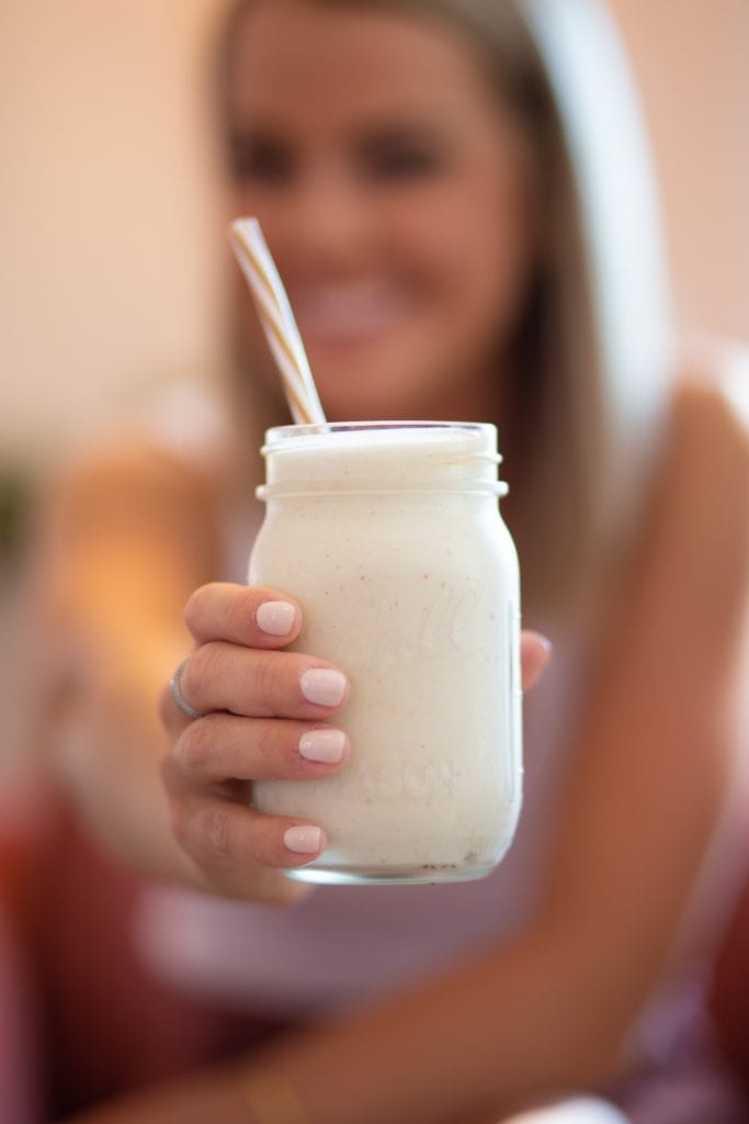 Woman holding a jar filled with cannabis infused banana smoothie Woman has pink nail polish and is out of focus in the background. a weed edible drink recipe.