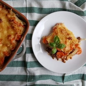 Breakfast casserole infused with cannabis in a cooking dish with a plate with a portion of the casserole on it all of this is on a striped kitchen towel