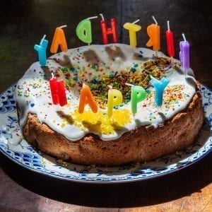 Edible birthday cake that has candles in it that say happy birthday on a blue plate on a wooden table