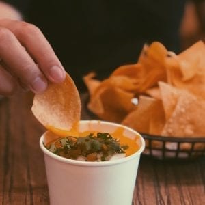 Person with a plate of tortilla chips dip in the chips into a container that has cannabis infused nacho cheese in it