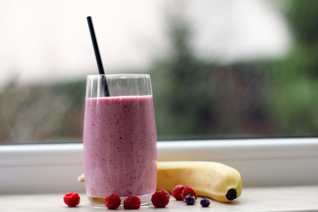 Cannabis strawberry smoothie with a black stripe in it on the table beside of banana raspberries blueberries. This is all on a window cell