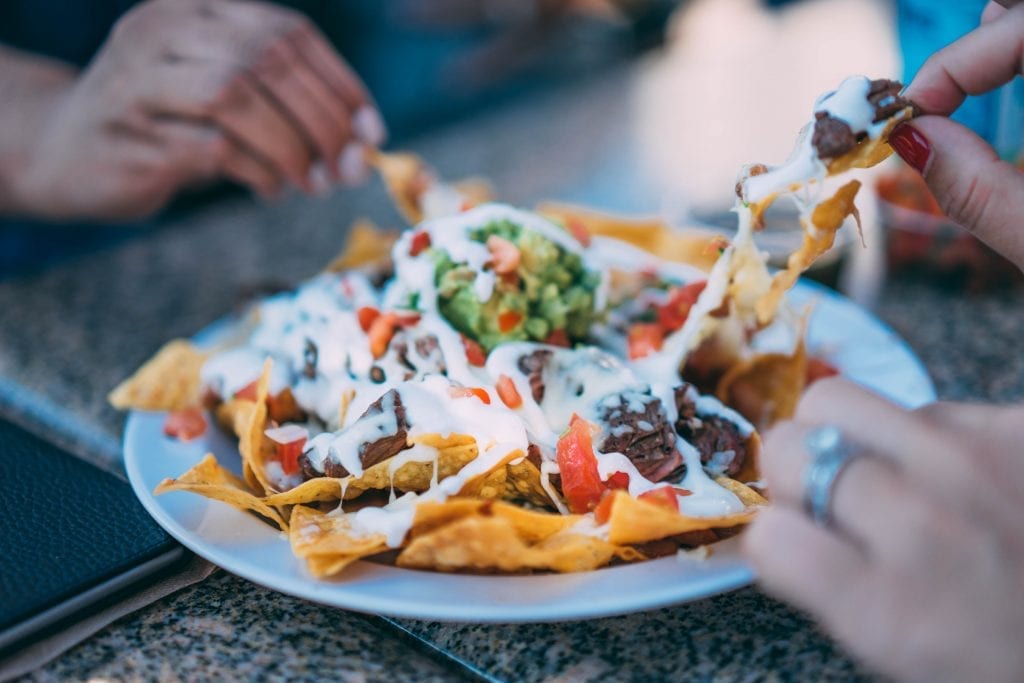 Two people sharing a plate of cannabis infused nachos nachos are garnished with green salsa cheese and sour cream