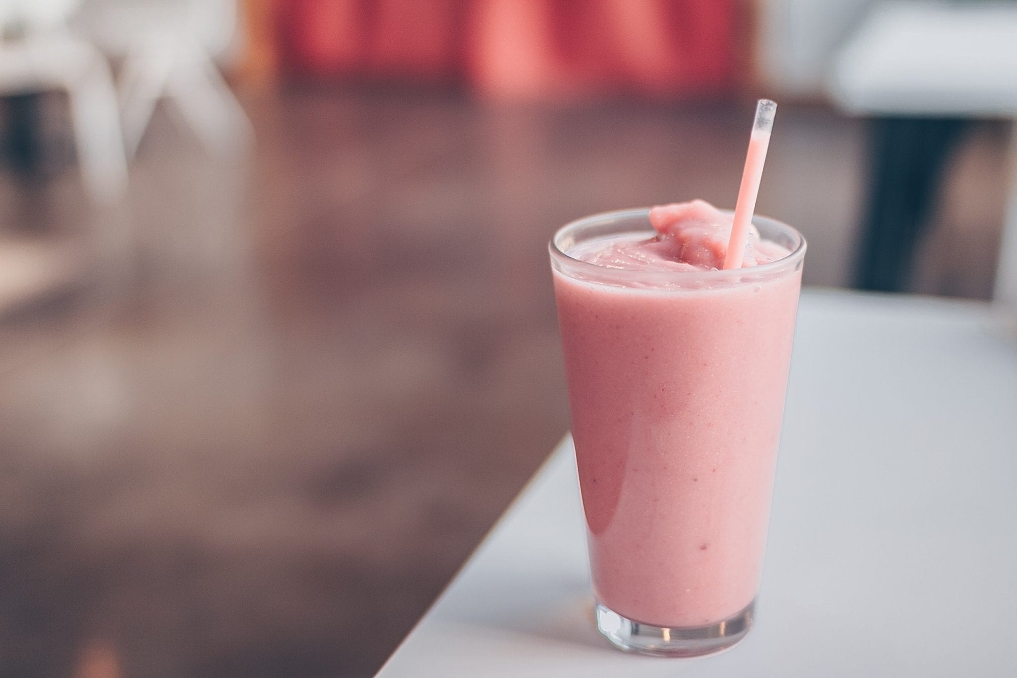 Edible strawberry smoothie on a white chair with brown floor in the background out of focus