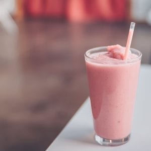 Edible strawberry smoothie on a white chair with brown floor in the background out of focus