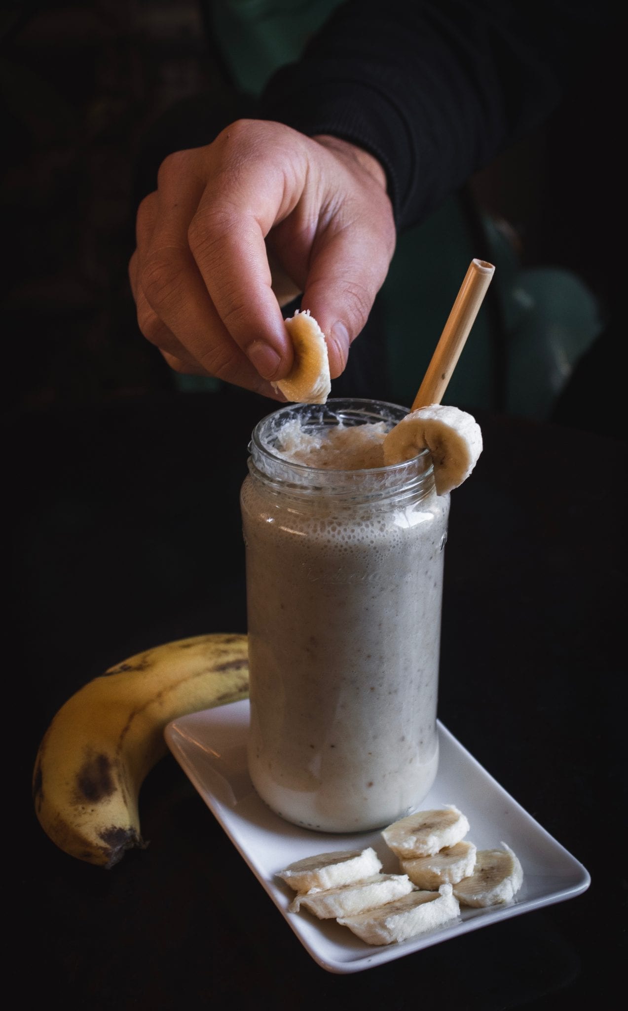 Cannabis banana milkshake on a plate with a persons hand dropping a banana into the milkshake