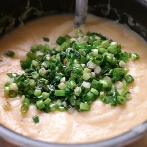 Cannabis potato soup in a pot with green onion on top of it the pot has a big spoon in it and its on a wooden cutting board