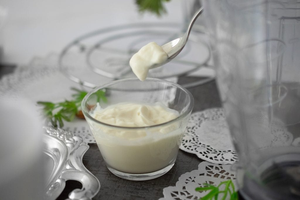 Infused yogurt on a grey table with a spoon taking a scoop out of it blender plates and other decorative items on the table too